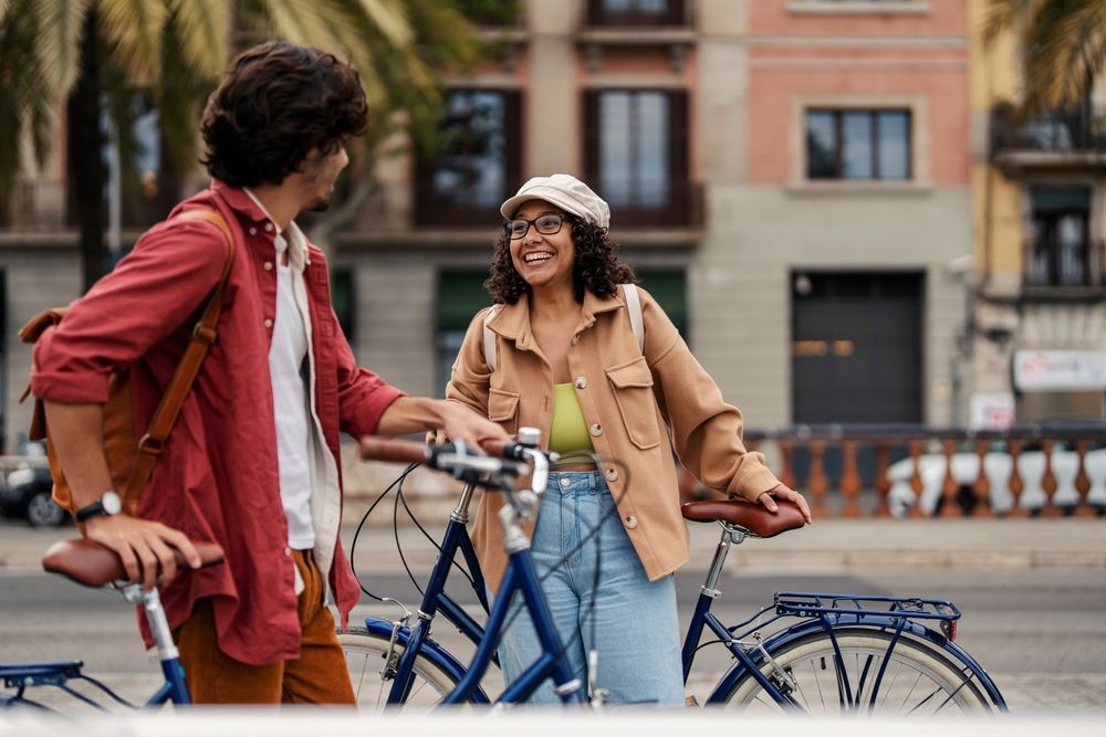 Dues persones somrient i xerrant mentre subjecten bicicletes en un carrer ampli amb arbres