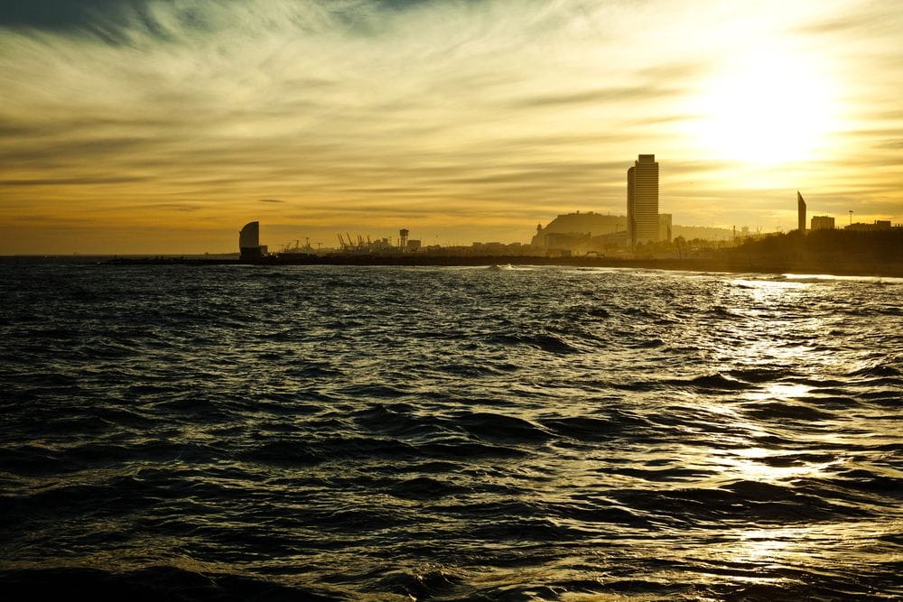 Silueta del litoral de Barcelona al capvespre vista des del mar, amb gratacels i el sol baix sobre l'aigua daurada