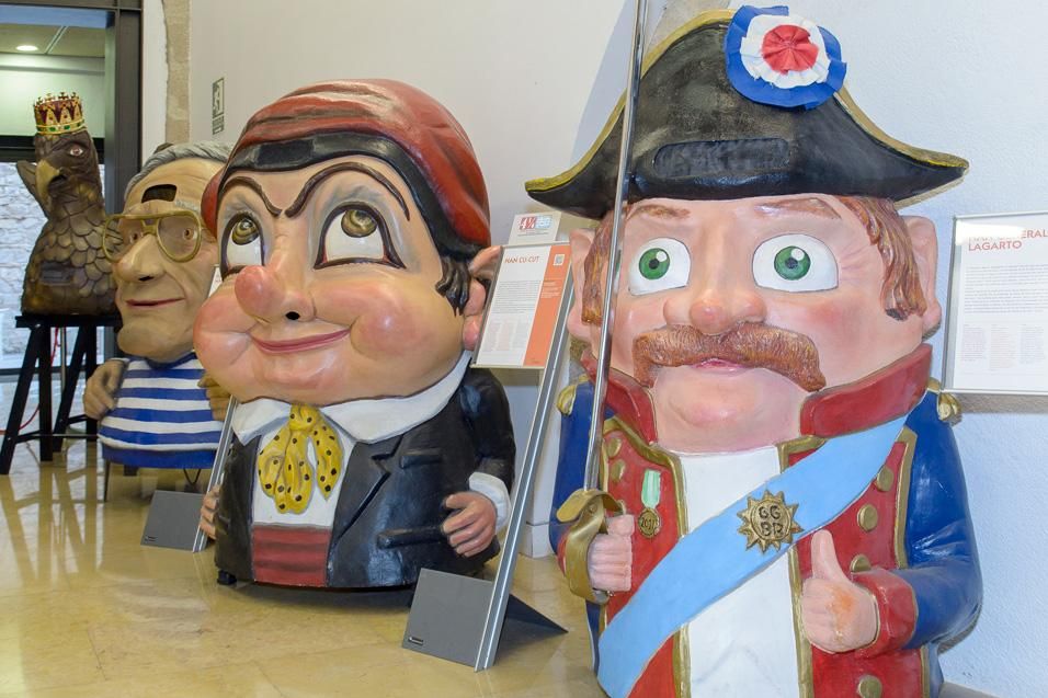 Figures de festa major de cap gran amb rostres pintats i vestits ornamentats exposades en un espai interior.