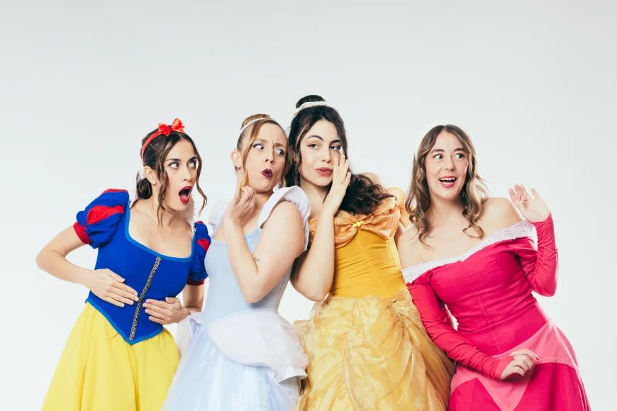 Quatre dones disfressades de princeses de conte amb vestits de colors —blau, blanc, groc i rosa— posant amb cara de sorpresa.