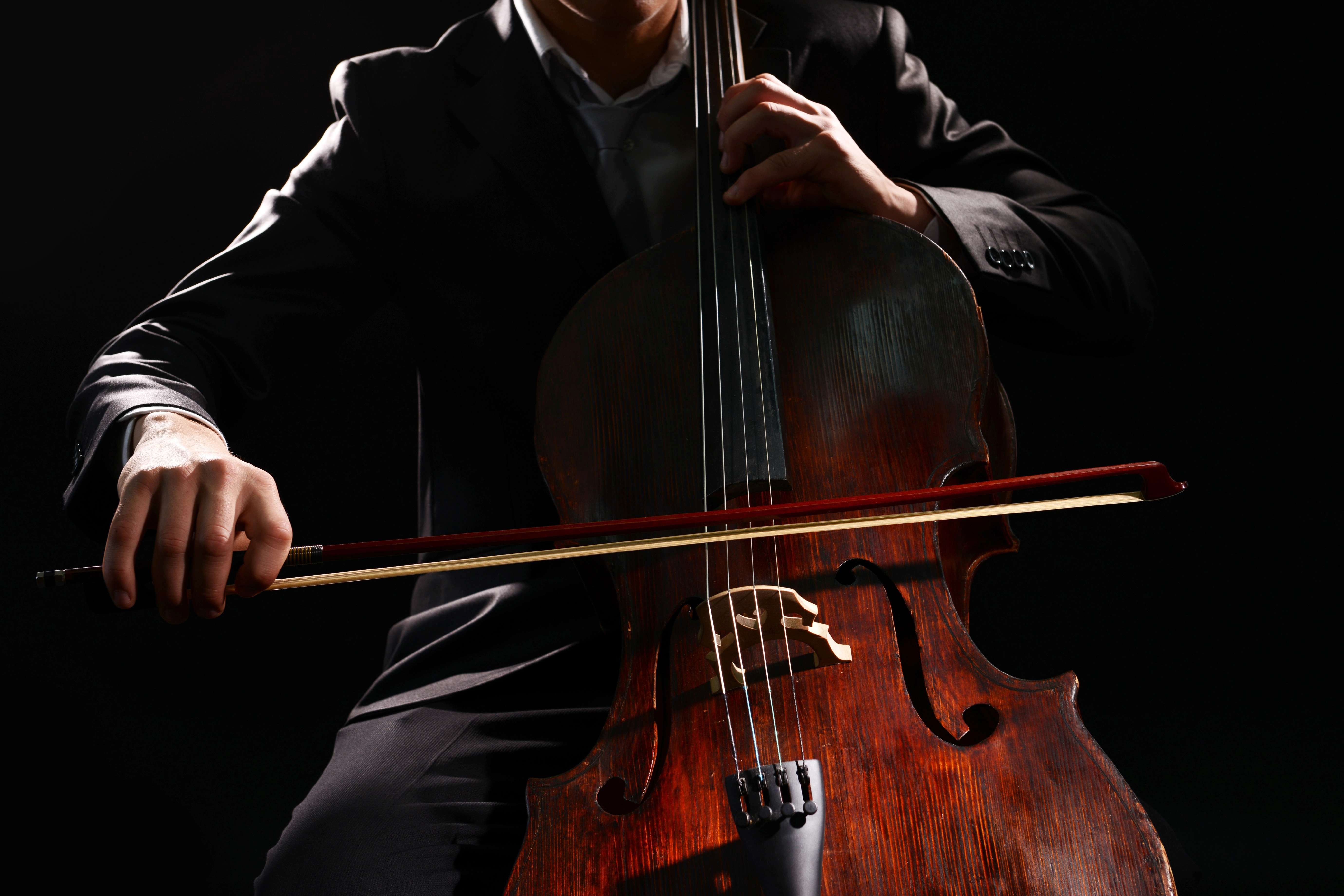 Músic vestit de fosc tocant un violoncel amb l'arquet, sobre fons negre