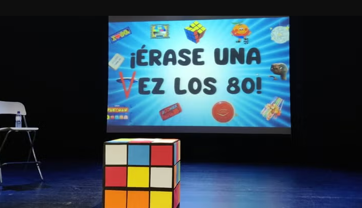 Escenari amb una pantalla projectada de colors i un cub de Rubik gegant al davant