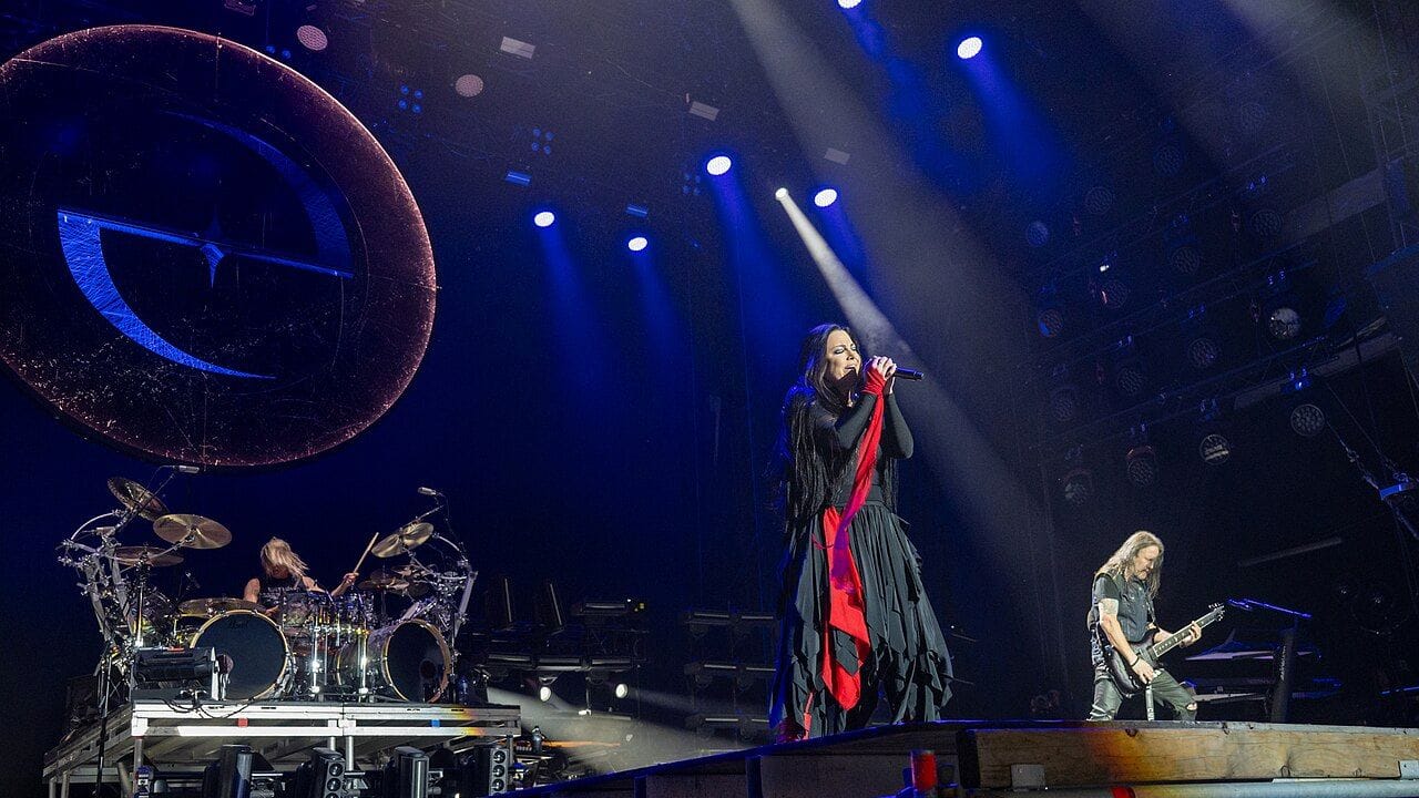 Cantant femenina amb vestit negre i vermell al centre d'un escenari il·luminat, acompanyada de guitarrista i bateria.