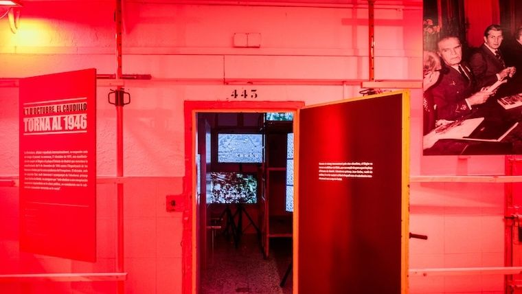 Espai expositiu immersiu amb parets i sostre vermells, una porta numerada i plafons amb textos i fotografies