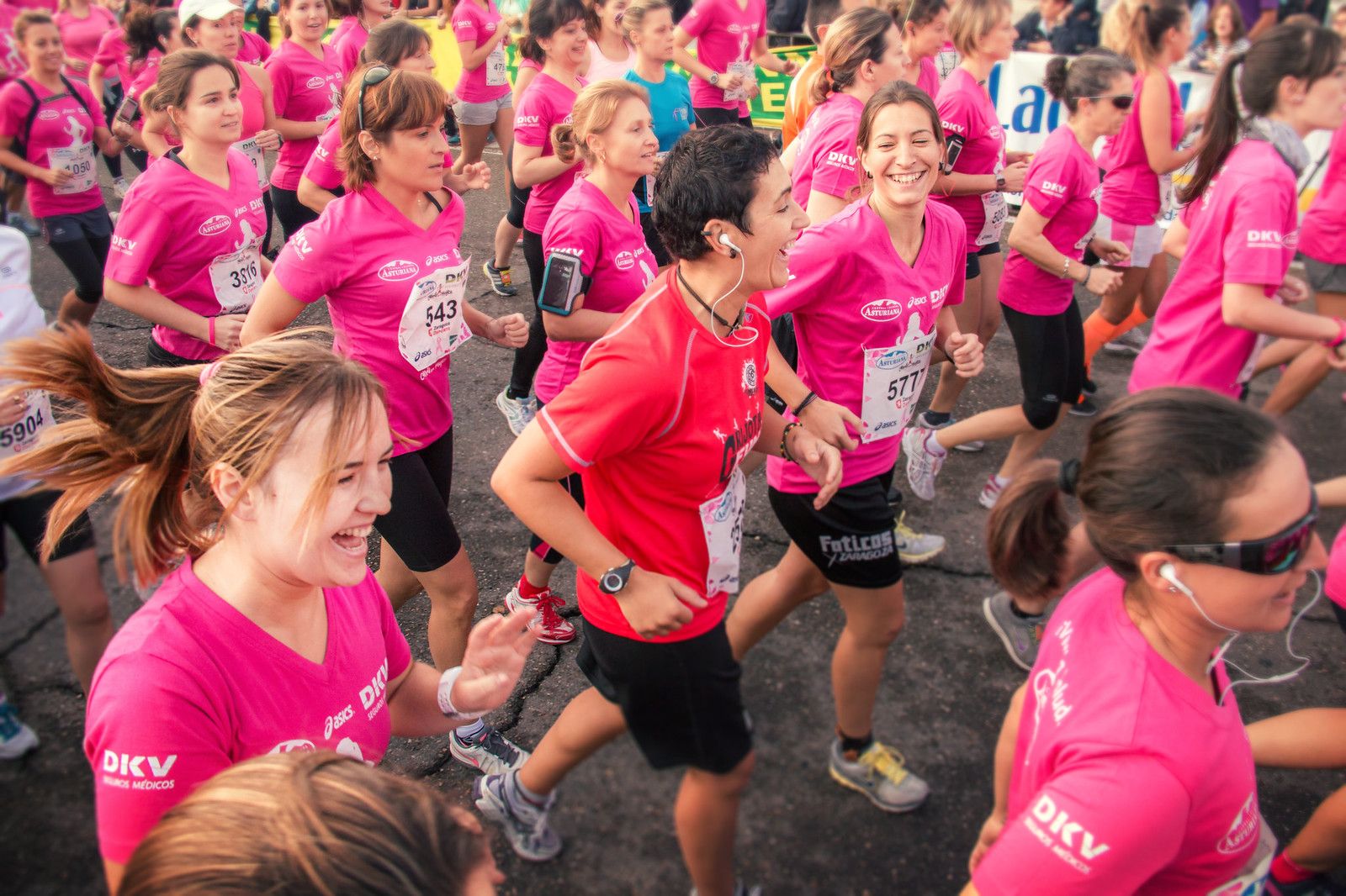 Grup de corredores amb samarretes roses corrent juntes somrients en una cursa popular a l'aire lliure