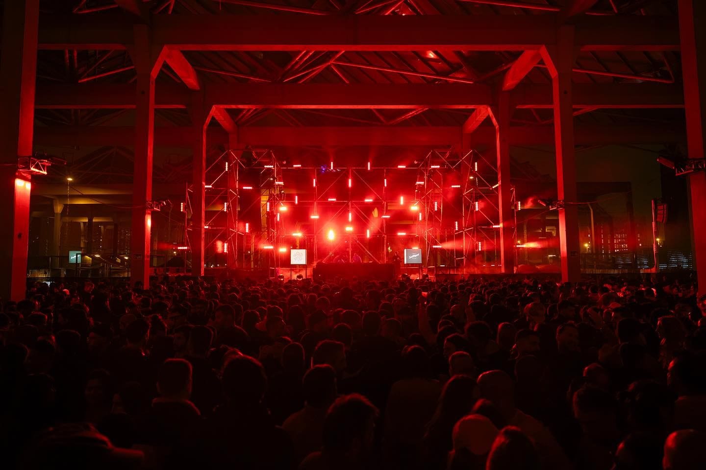 Multitud davant d'un escenari amb llums vermells en un recinte industrial cobert