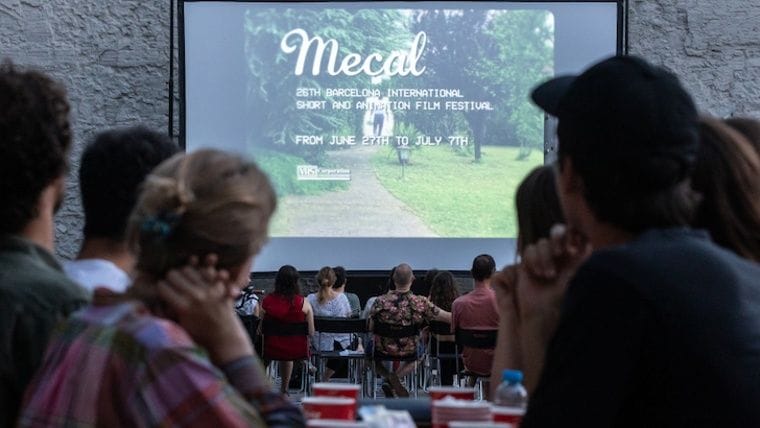 Cinema a l'aire lliure al capvespre: espectadors asseguts davant una gran pantalla de projecció entre arbres