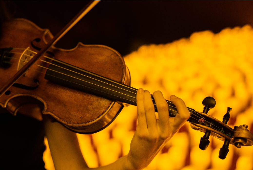 Primer pla d'un violí tocant-se, amb un fons borrós de llums daurades d'espelmes
