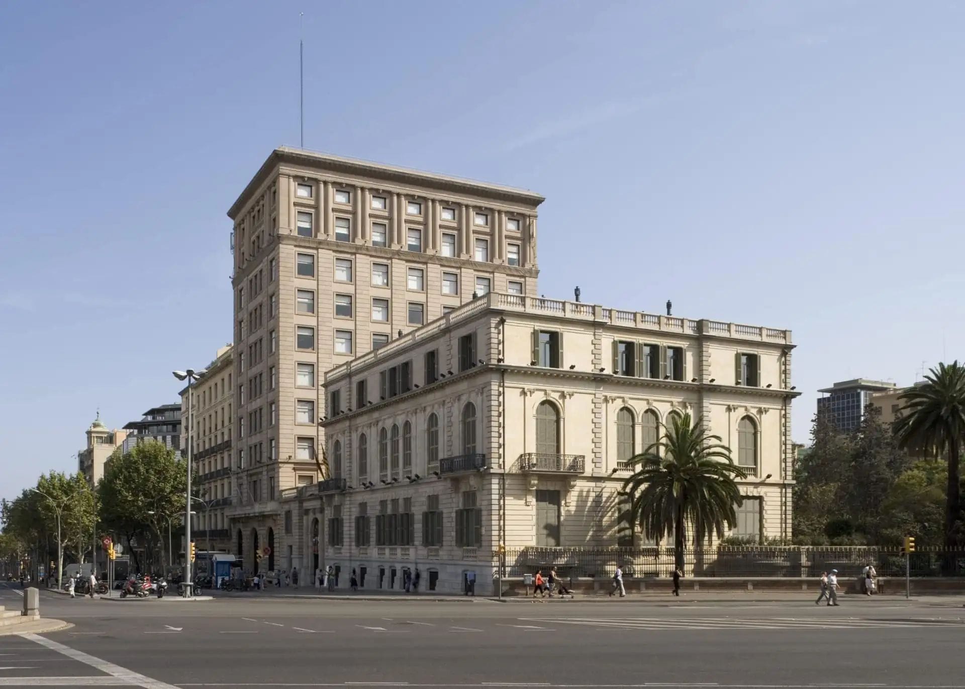 Edifici institucional de principis del segle XX amb façana neoclàssica fotografiat des d'una avinguda àmplia amb palmeres i vianants.