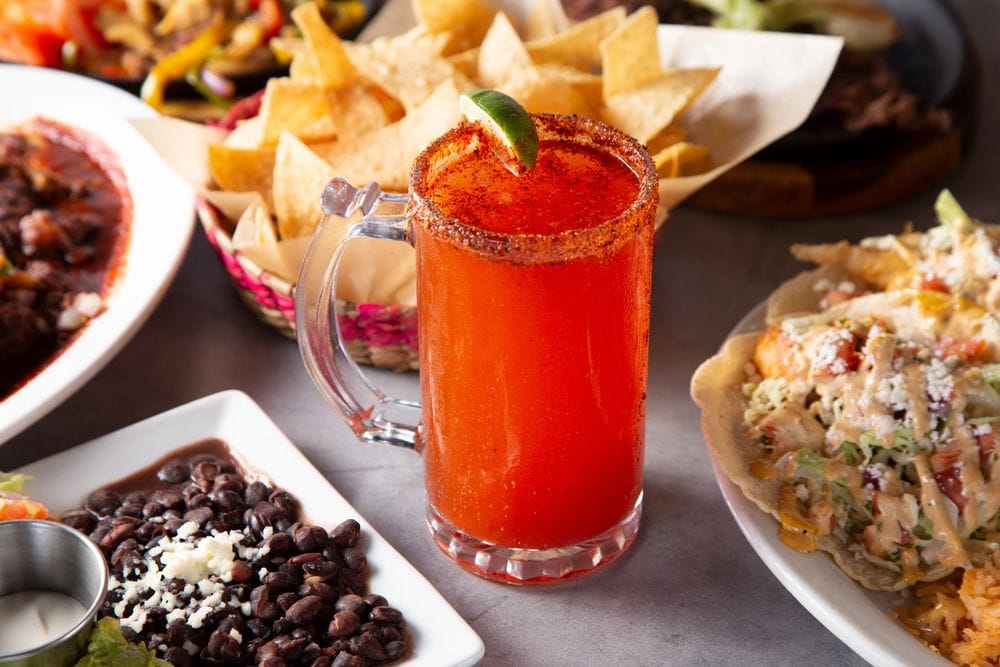 Got de michelada amb la vora especiada i una llima, envoltat de nachos, una tostada i un plat de mongetes negres
