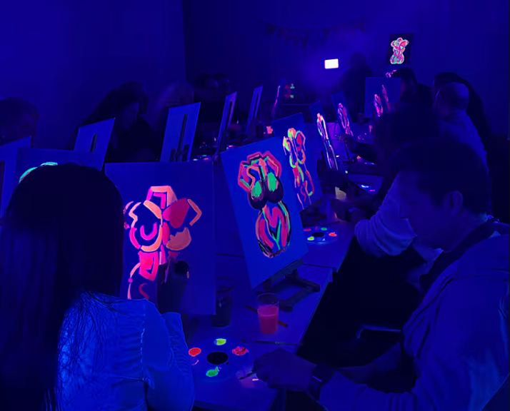 Persones pintant teles amb pintura fluorescent que brilla sota llum negra en una sala fosca