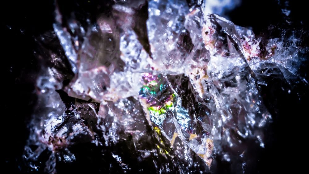 Primer pla d'una superfície mineral cristal·lina amb reflexos iridescents en tons morats, blaus i rosats sobre fons fosc.