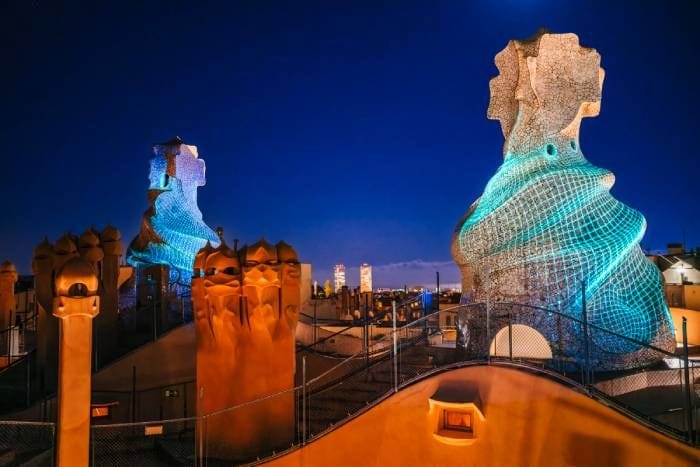 Terrassa amb xemeneies escultòriques il·luminades de nit en blau i taronja, amb el cel nocturn al fons