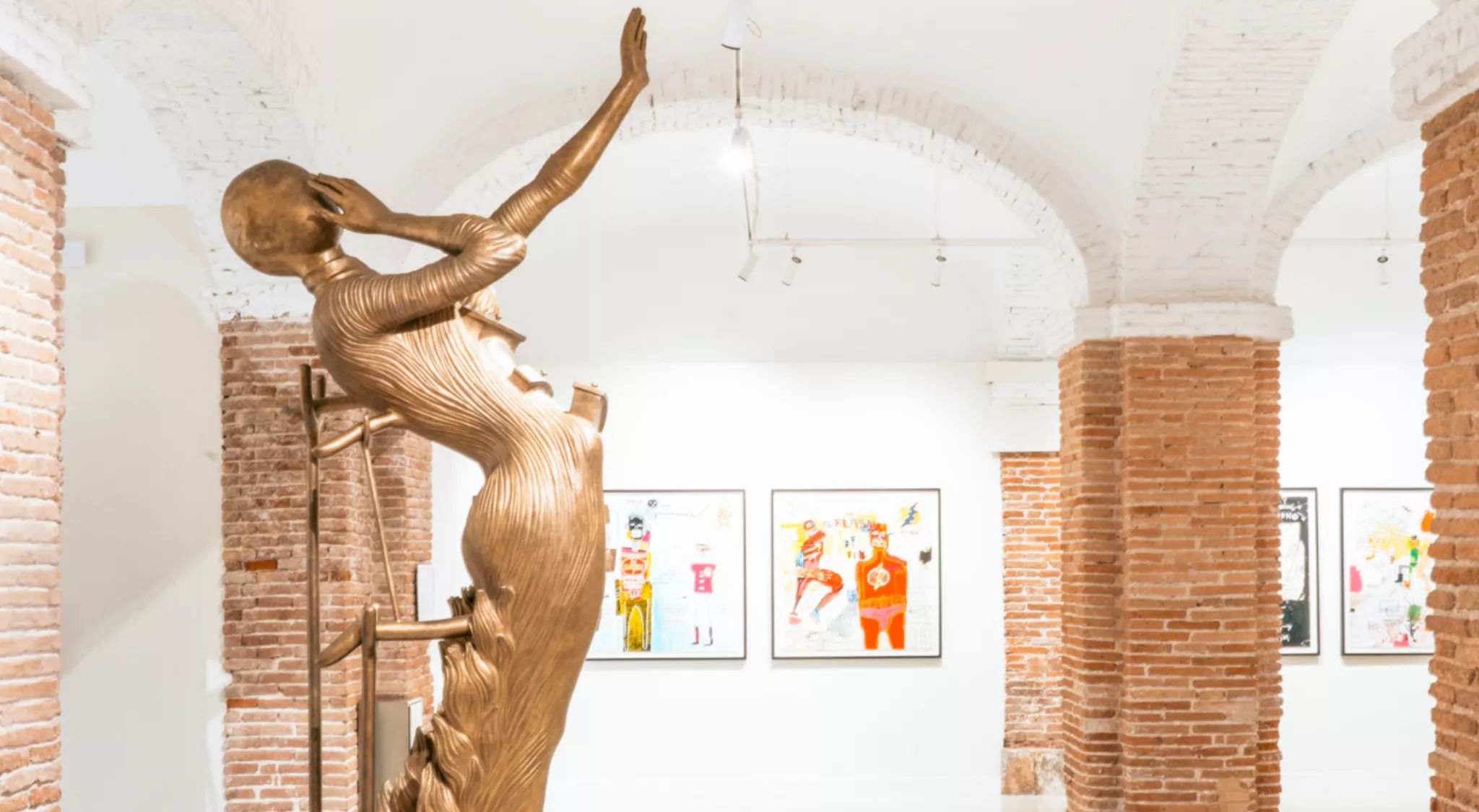 Sala d'exposicions amb sostre de maó i columnes, una gran escultura daurada al centre i pintures colorides a les parets