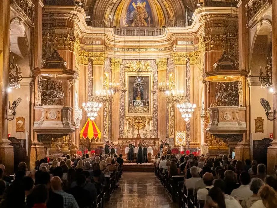 Concert d'un grup de músics davant l'altar daurat d'una església barroca, amb el públic assegut als bancs