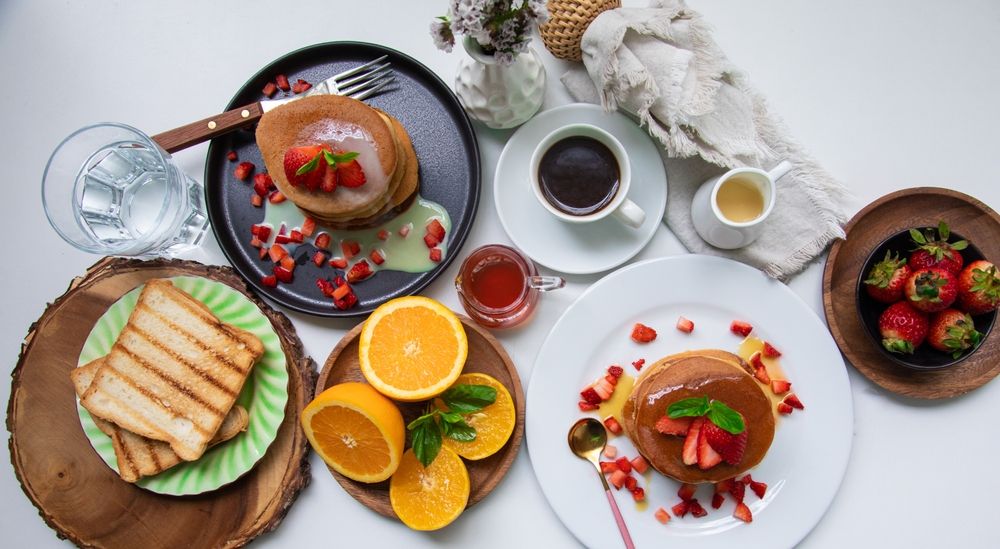 Vista cenital d'una taula de brunch amb plats variats, fruita tallada, sandvitxos i una tassa de cafè