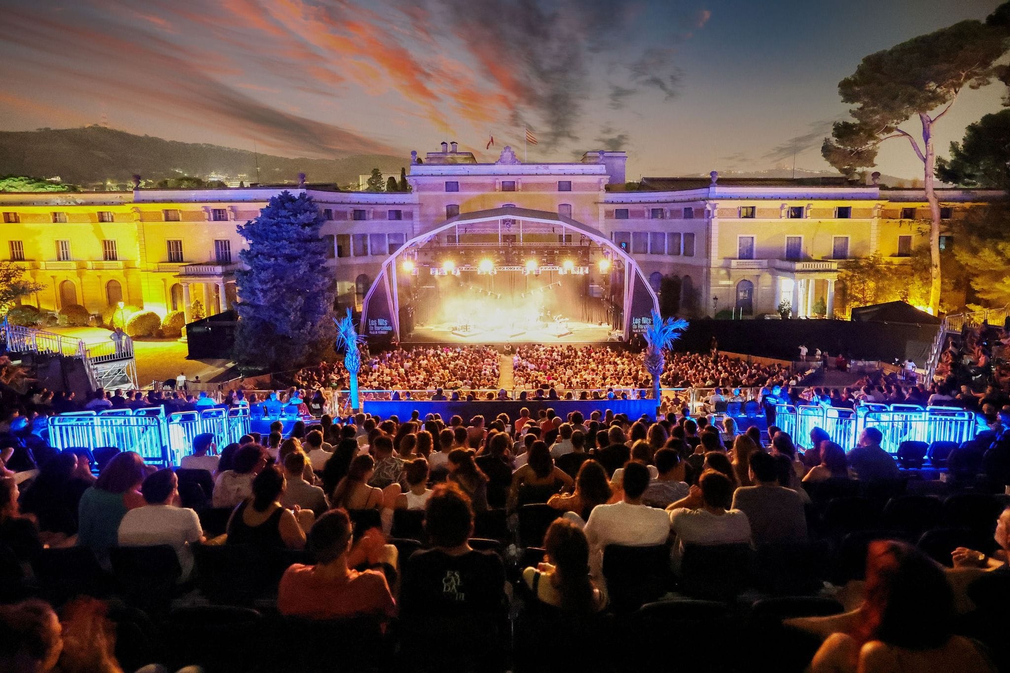 Concert a l'aire lliure de nit en un jardí neoclàssic il·luminat, amb públic assegut i un escenari al fons
