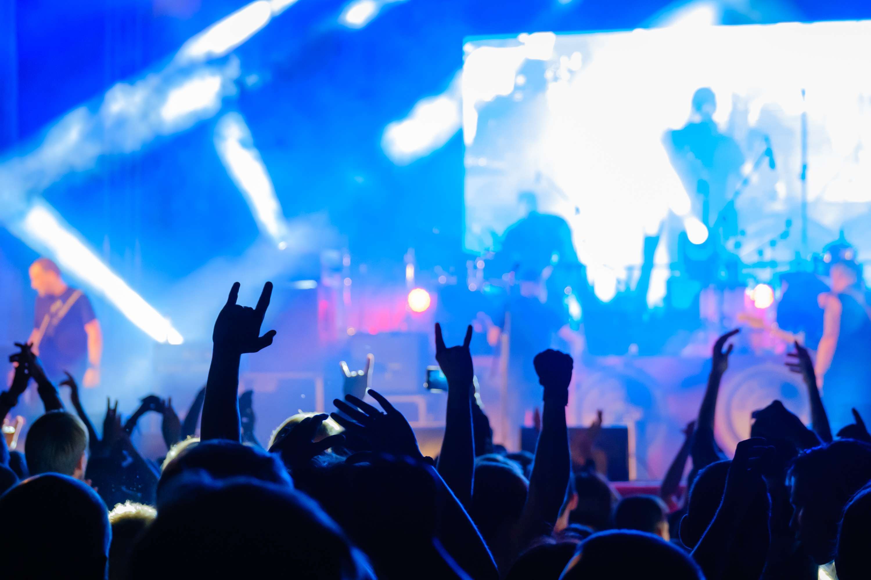 Públic d'un concert de rock amb les mans alçades fent el gest de les banyes, davant un escenari amb llums blaves i fum