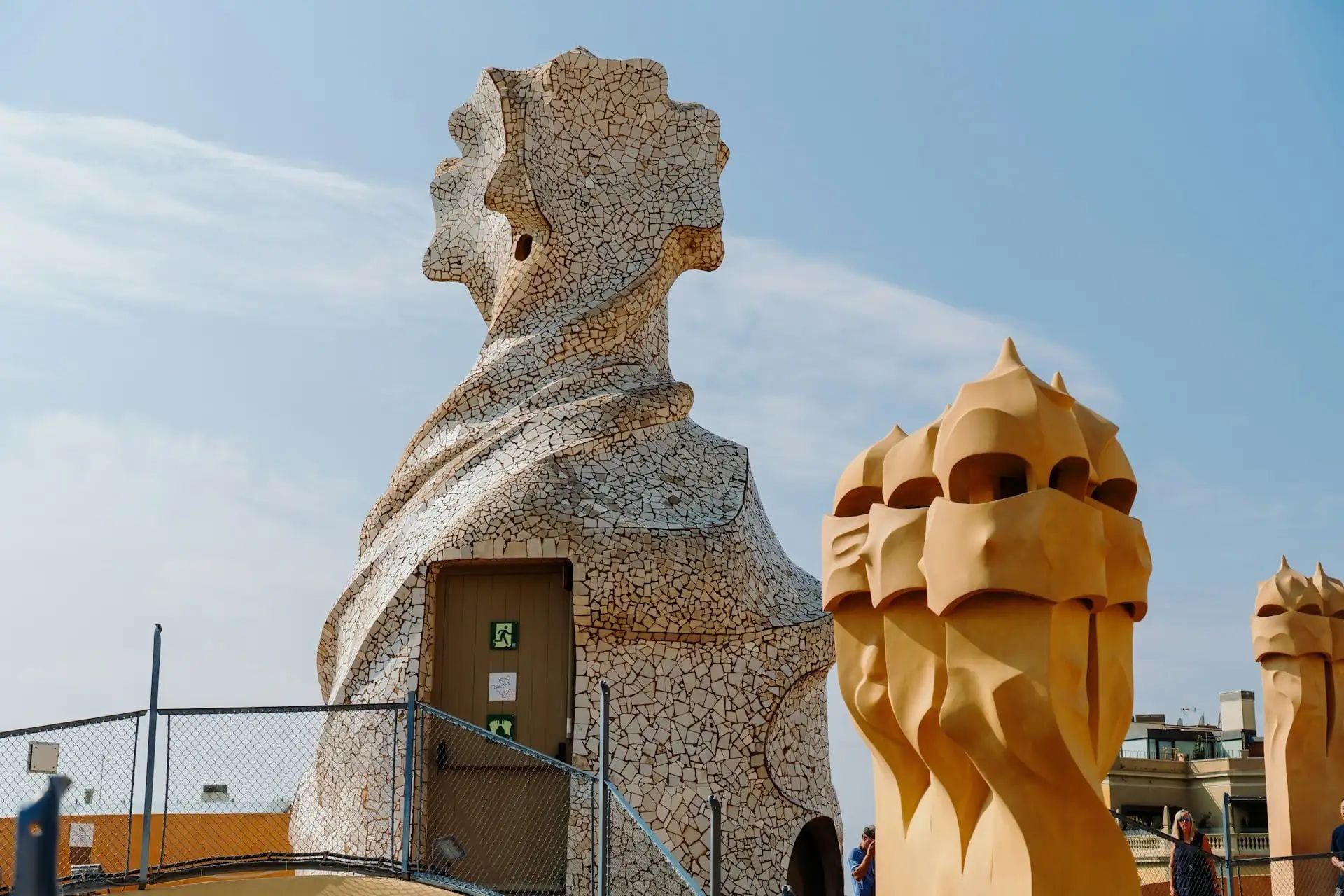 Terrassa superior d'un edifici modernista amb xemeneies i conductes de ventilació esculpits en pedra de formes orgàniques sota un cel blau.