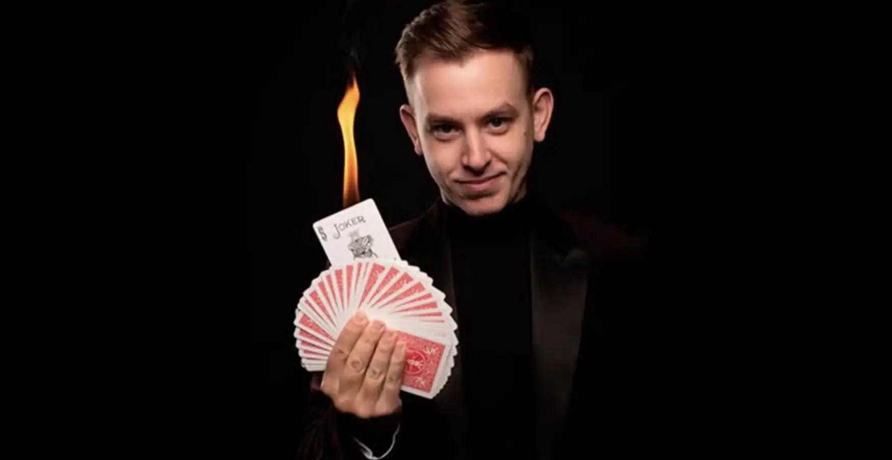 Home de vestit negre sostenint un ventall de cartes de joc amb una flama al fons fosc