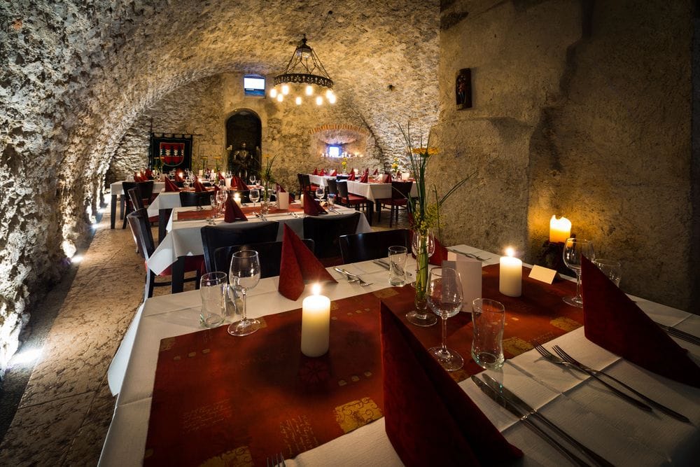 Sala de sopar amb voltes de pedra, espelmes sobre les taules i comensals asseguts